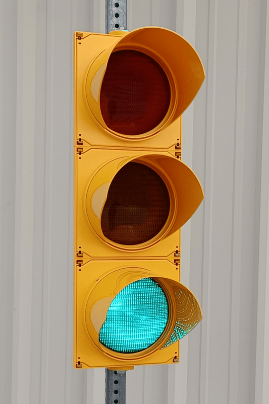 Yellow 3-section ITE traffic signal head mounted on pole with green LED lens illuminated"